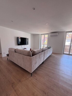 A spacious living room with a large sofa, a flat-screen TV mounted on the wall, and a sliding glass door leading to an outdoor area. - New Listing (Saint-Raphaël)