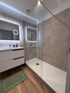 A modern bathroom with a glass-enclosed shower, a vanity with a mirror, and a green rug on the floor. - New Listing (Saint-Raphaël)