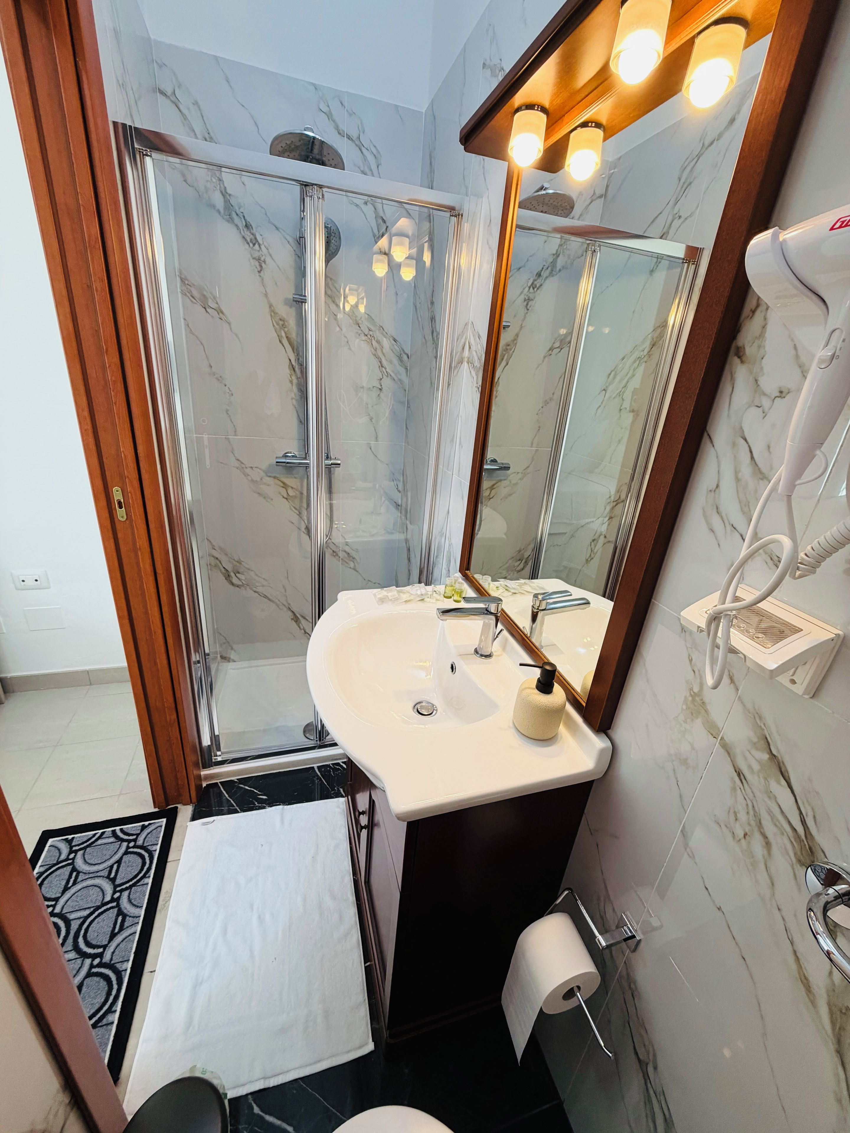 Un baño con cabina de ducha de vidrio, un lavamanos blanco con espejo y un perchero para toallas.
