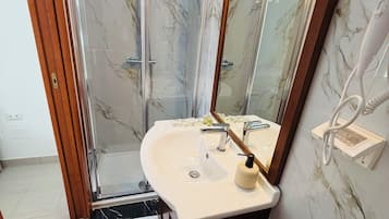 Un baño con cabina de ducha de vidrio, un lavamanos blanco con espejo y un perchero para toallas.