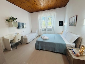 Habitación de hotel con cama, escritorio, silla, televisor, ventana con cortinas y mesita de noche con lámpara.