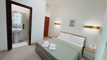 Habitación de hotel con cama, mesitas de noche, lámpara de pared, un cuadro de la Torre inclinada de Pisa y un baño visible a través de una puerta abierta.