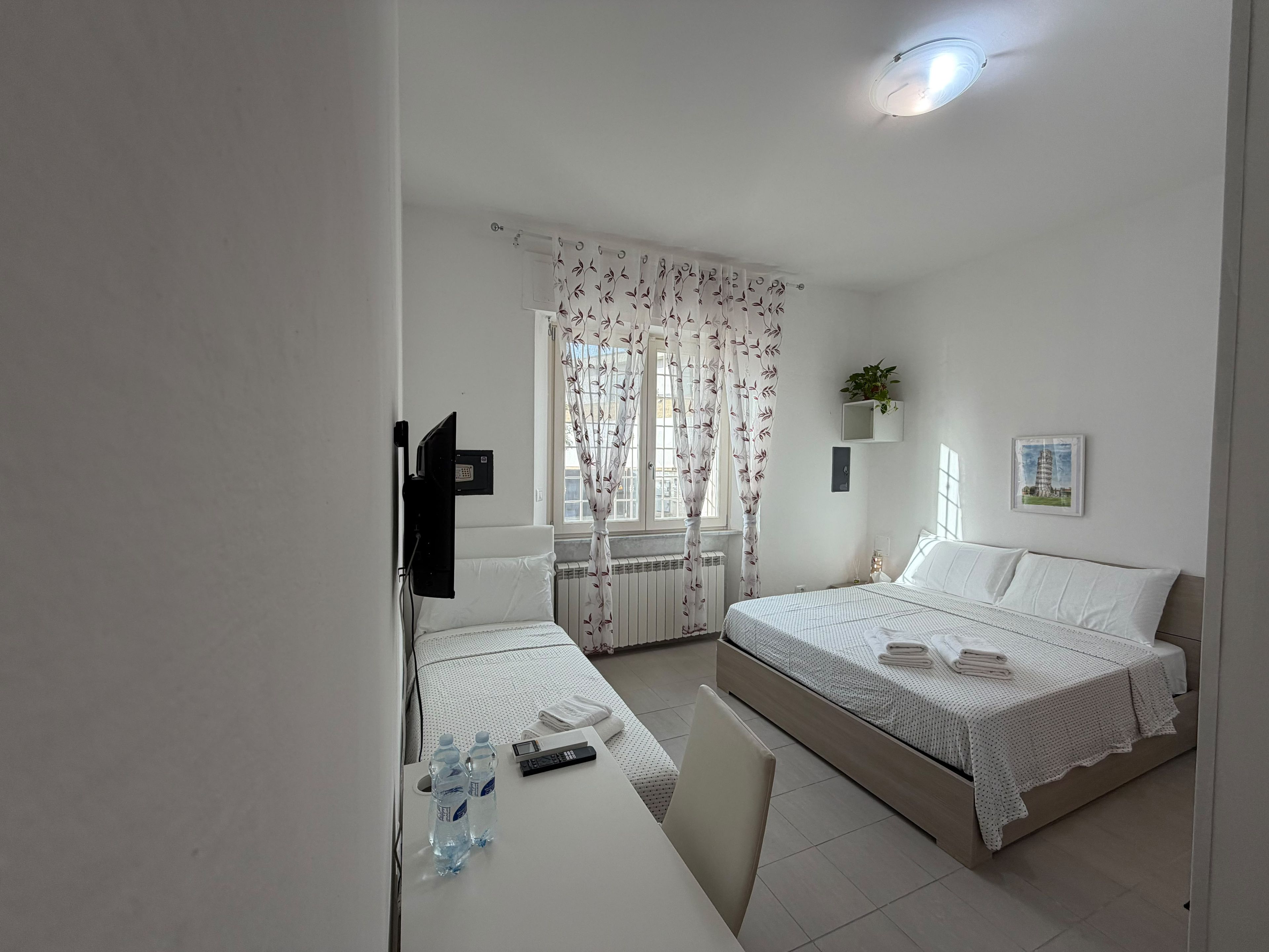 A hotel room with a bed, bedside table, chair, and a window with curtains.