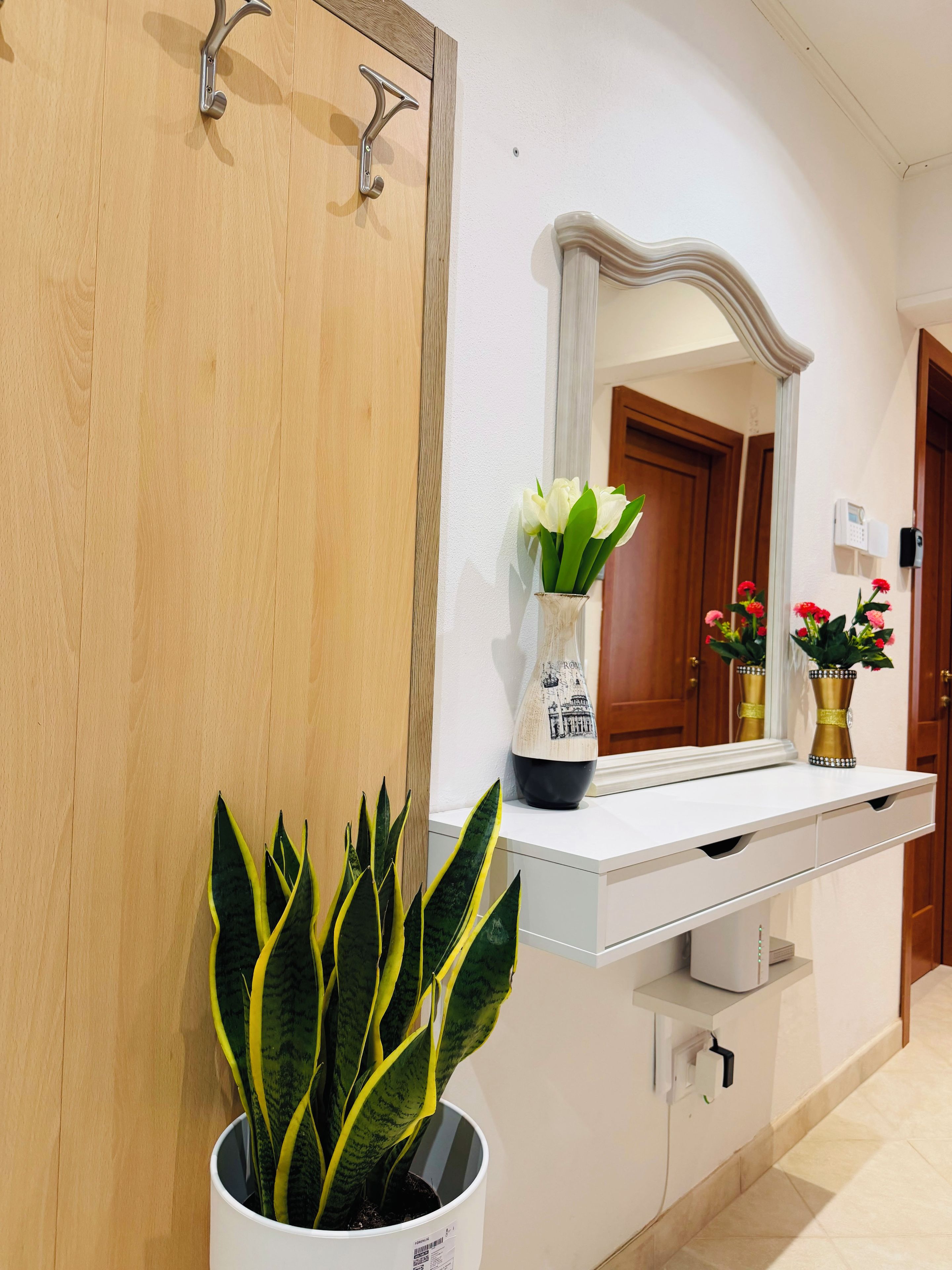 Une salle de bain avec une porte en bois, un lavabo blanc avec un miroir au-dessus, et une plante en pot aux feuilles vertes.