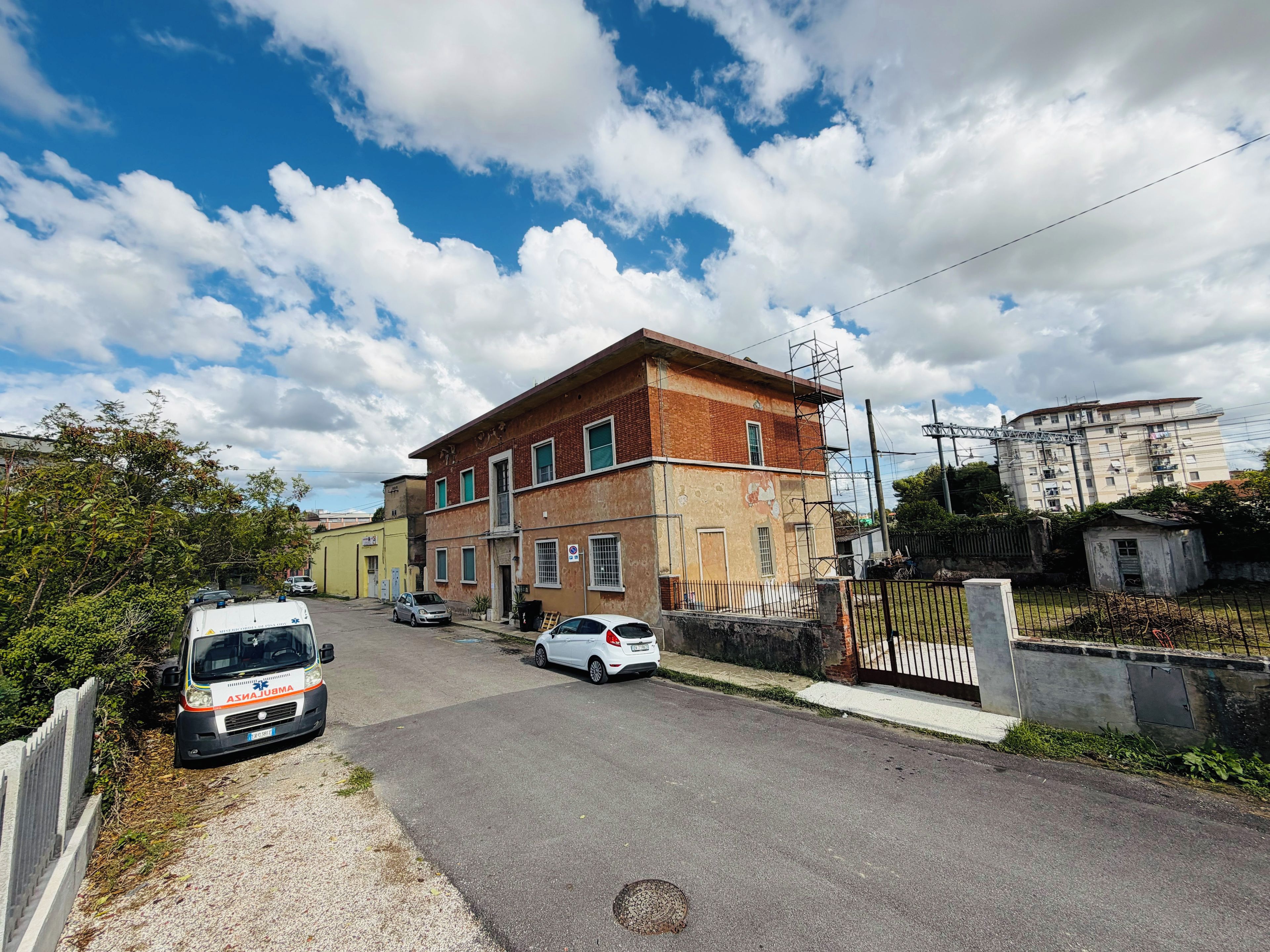 Vista callejera con un edificio en construcción, una ambulancia estacionada y un área cercada.