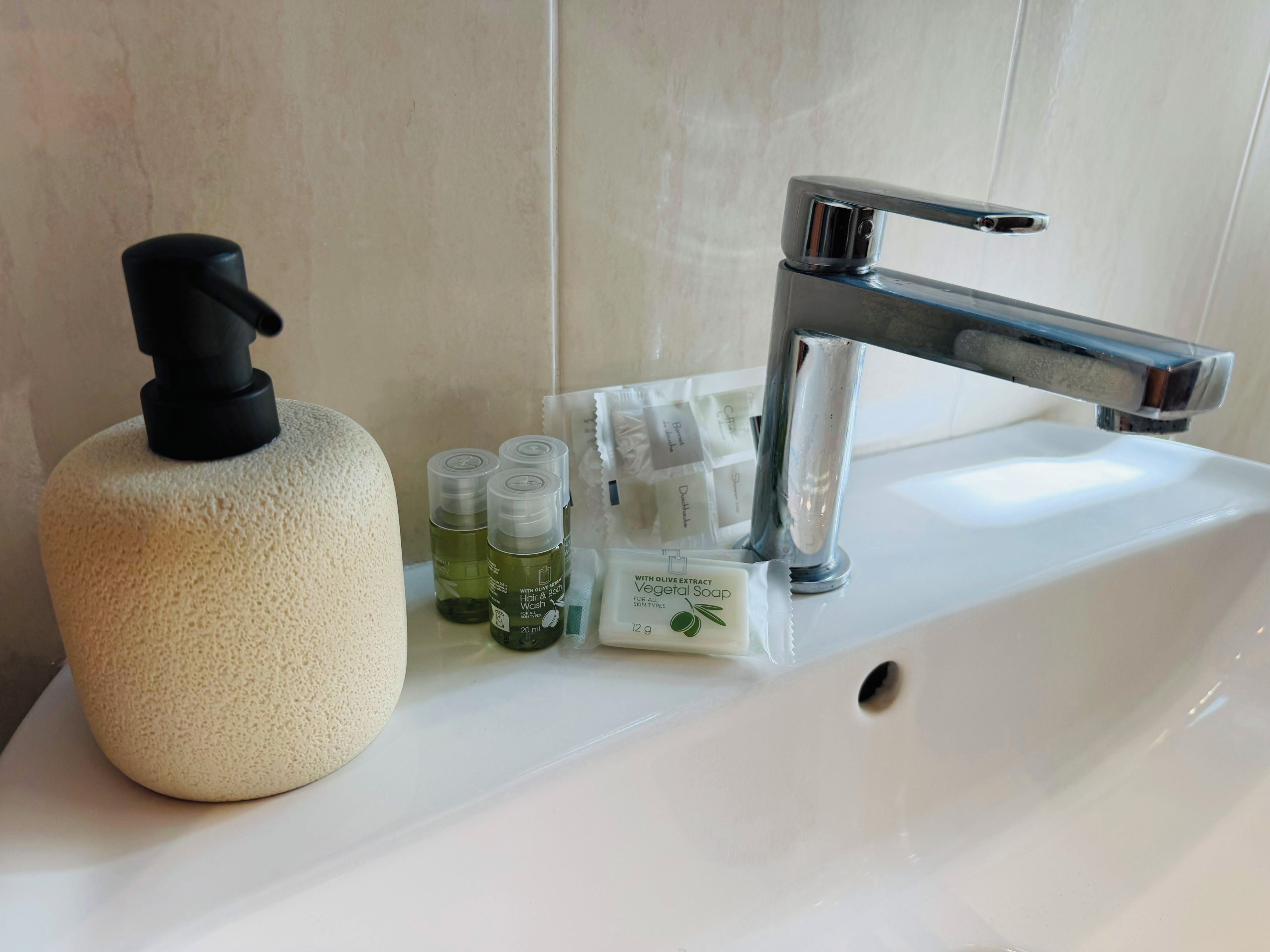 A bathroom sink with a soap dispenser, a bottle of olive oil soap, and a few small bottles of liquid soap.
