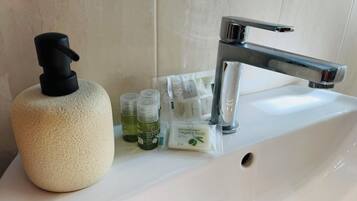A bathroom sink with a soap dispenser, a bottle of olive oil soap, and a few small bottles of liquid soap.