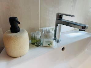 Un lavabo de salle de bain avec un distributeur de savon, une bouteille de savon à l’huile d’olive et quelques petites bouteilles de savon liquide.