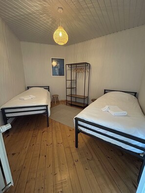 A bedroom with two single beds, a wooden floor, a hanging light fixture, and a coat rack. - New Listing (De Panne)
