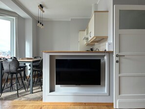 A modern kitchen with a built-in TV, wooden flooring, and a dining area with chairs. - New Listing (De Panne)