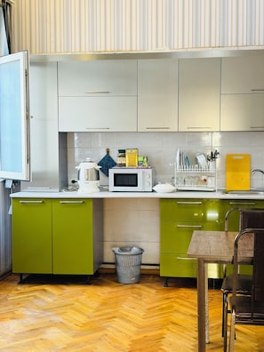 A kitchen with green cabinets, a microwave, a sink, and a wooden dining table. - Alina Central Hostel (Baku)