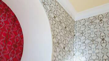 Een kamer met een gebogen muur, een bed met witte lakens, behang met een patroon en een raam met gezoet glas.