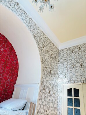 A room with a curved wall, a bed with white bedding, a patterned wallpaper, and a window with frosted glass. - Alina Central Hostel (Baku)