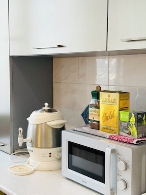 Una cocina con cafetera, microondas y cajas de té sobre la encimera.