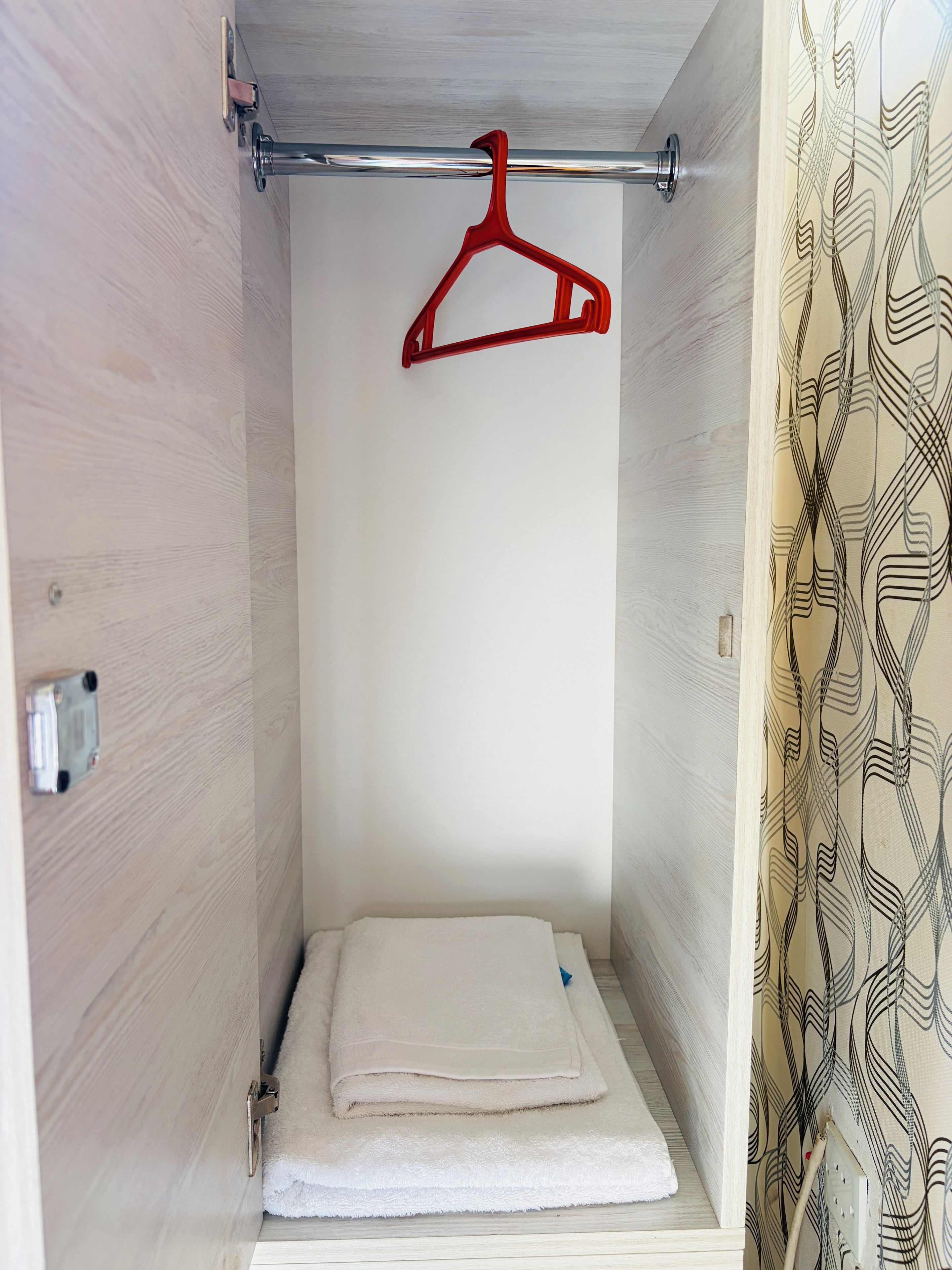 A small, enclosed space with a metal rod, a red hanger, and a folded white towel on a shelf.