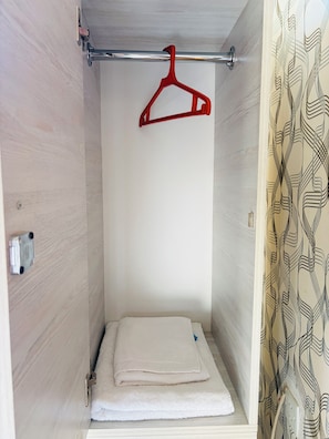 A small, enclosed space with a metal rod, a red hanger, and a folded white towel on a shelf. - Alina Central Hostel (Baku)