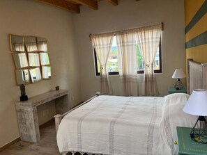 A bedroom with a bed, a bedside table with a lamp, a mirror on the wall, and a window with curtains.