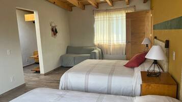A bedroom with two beds, a wooden ceiling, a window with curtains, and a bedside table with lamps.
