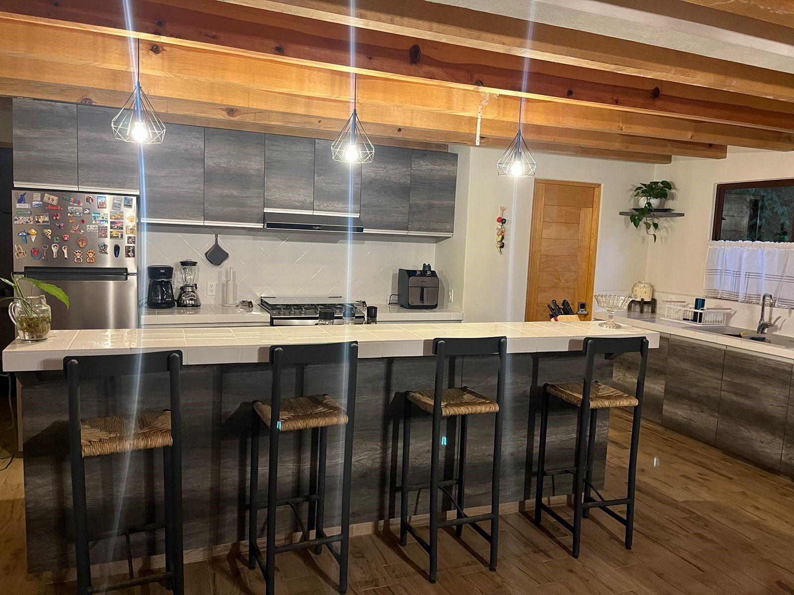 A modern kitchen with a central island, bar stools, and pendant lighting.