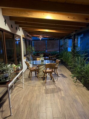 An outdoor dining area with a glass table surrounded by wooden chairs, under a wooden pergola with string lights. - New Listing (San Mateo Acatitlán)