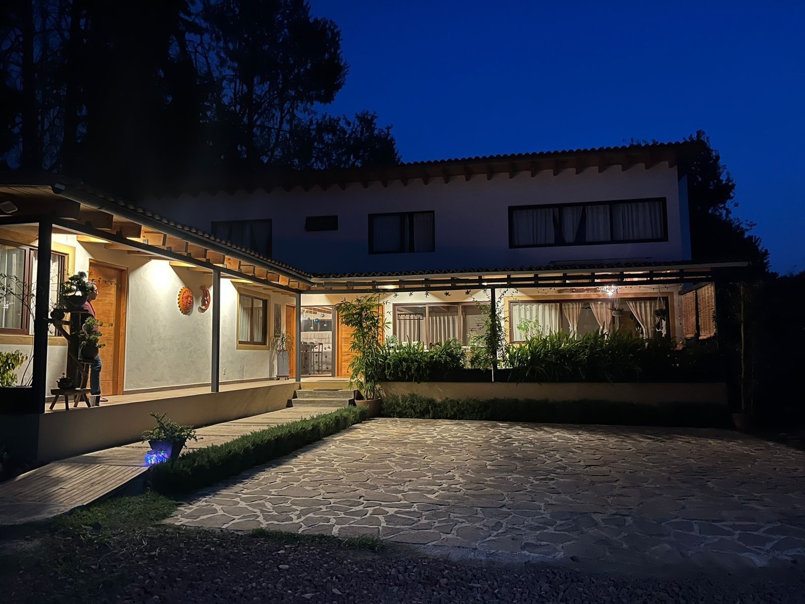 A two-story house with a stone courtyard, a covered patio, and a well-lit entrance.