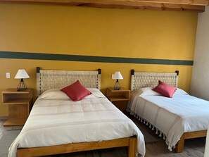 Two single beds with wooden frames and woven headboards, each with a bedside table and lamp, in a room with yellow walls and a green stripe. - New Listing (San Mateo Acatitlán)