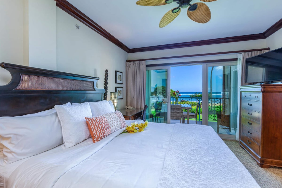 A hotel room with a large bed, a television, and a view of the ocean through the balcony doors.