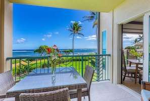 A balcony with a clear view of the ocean, a table with chairs, and a tropical garden. - Shoshone Condominums (Big Sky)