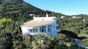 A modern two-story house with a balcony, surrounded by lush greenery and hills. - Mythos Luxury  rooftop duplex  apatment with panoramic view (Corfu)