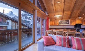 A cozy interior with a dining area, a sofa with cushions, and large windows offering a mountain view. - THREE-BEDROOM ZERMATT RETREAT WITH VIEWS OF VILLAGE & MATTERHORN (Zermatt)