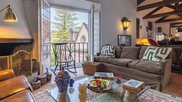A cozy living room with a leather sofa, a glass coffee table with decorative items, a fireplace, and a view of a building outside.