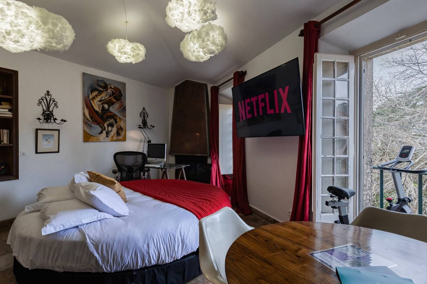 A hotel room with a bed, a desk, a computer, a TV, and a balcony with exercise equipment.