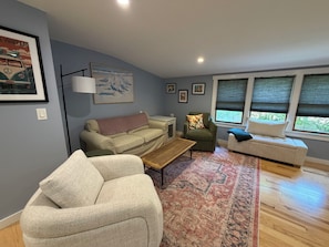A living room with a beige sofa, a green armchair, a coffee table, and a patterned rug. - Relaxing Vineyard Retreat, FREE CAR, Fenced yard, Pet Friendly, Sleeps 10! (West Tisbury)