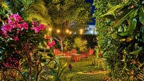 An outdoor garden area with a dining setup featuring chairs and tables, surrounded by lush greenery and flowering plants. - Casa Arcos - Coastal Escape - Entire House & Attached Apartment 5 Min Beach Walk (Playa Hermosa)