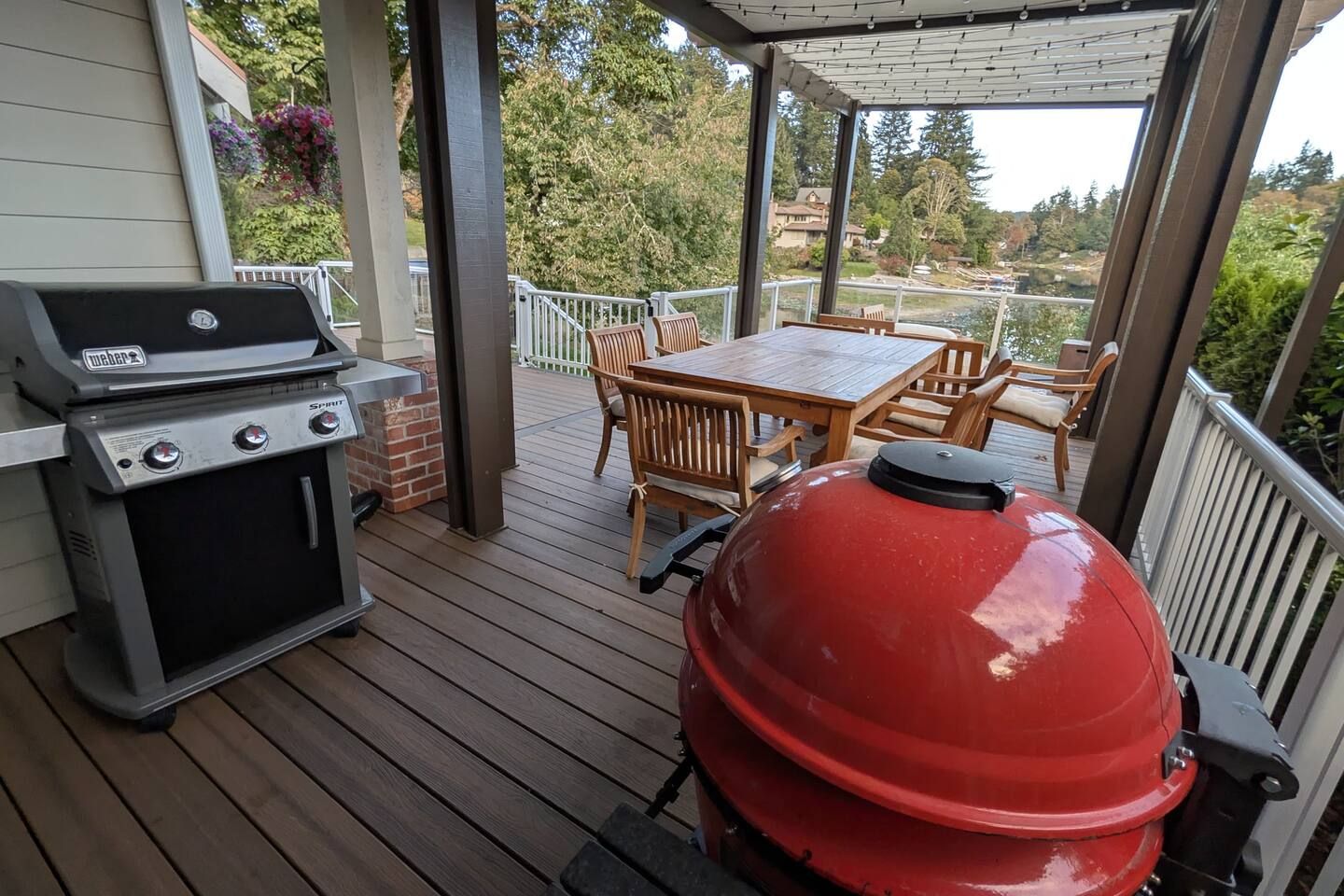 Une terrasse extérieure couverte, équipée d’un barbecue Weber Spirit, d’un fumoir Weber rouge et de mobilier en bois.