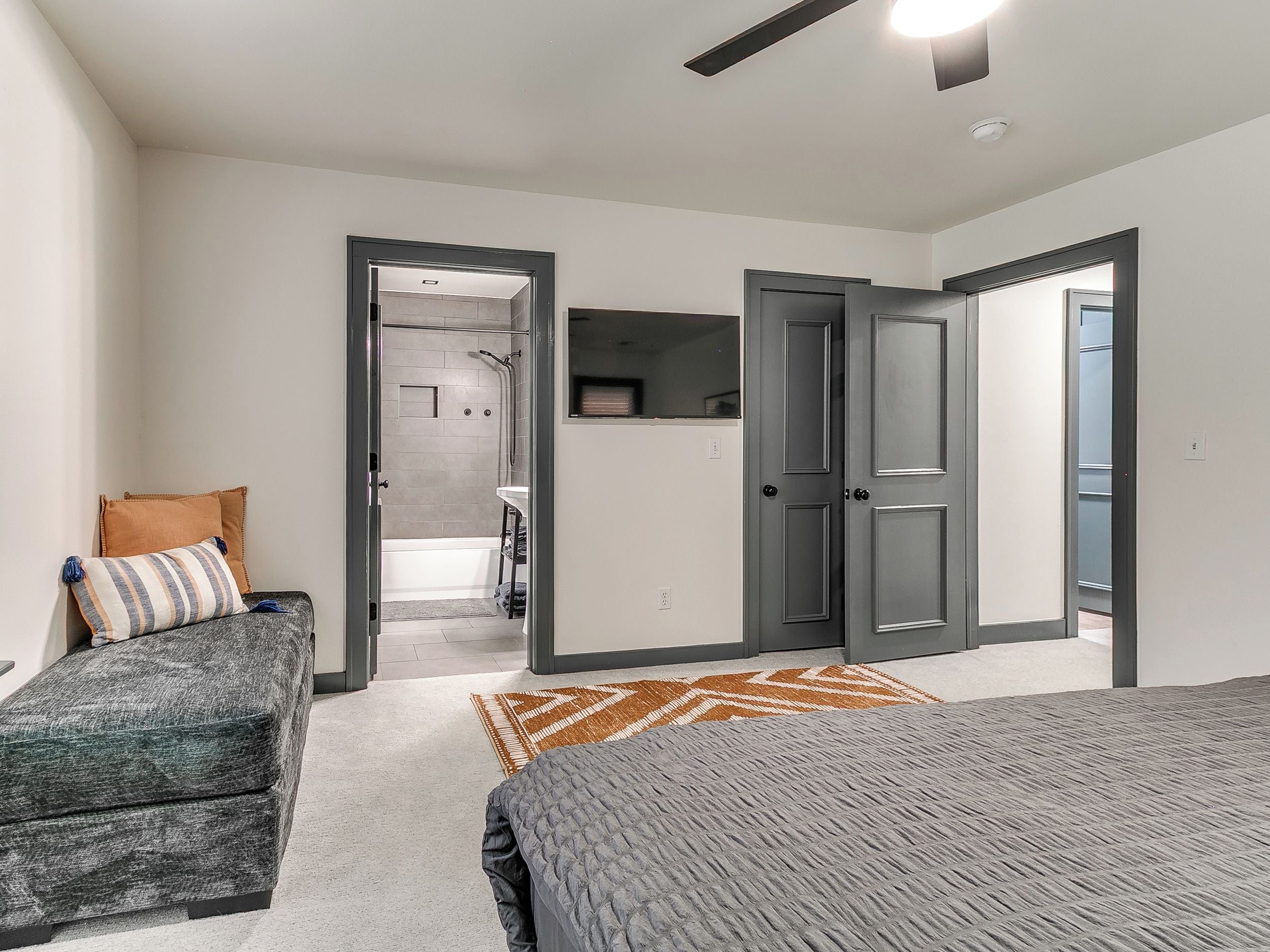 A bedroom with a bed, a sofa, a shower area, and a door leading to another room.