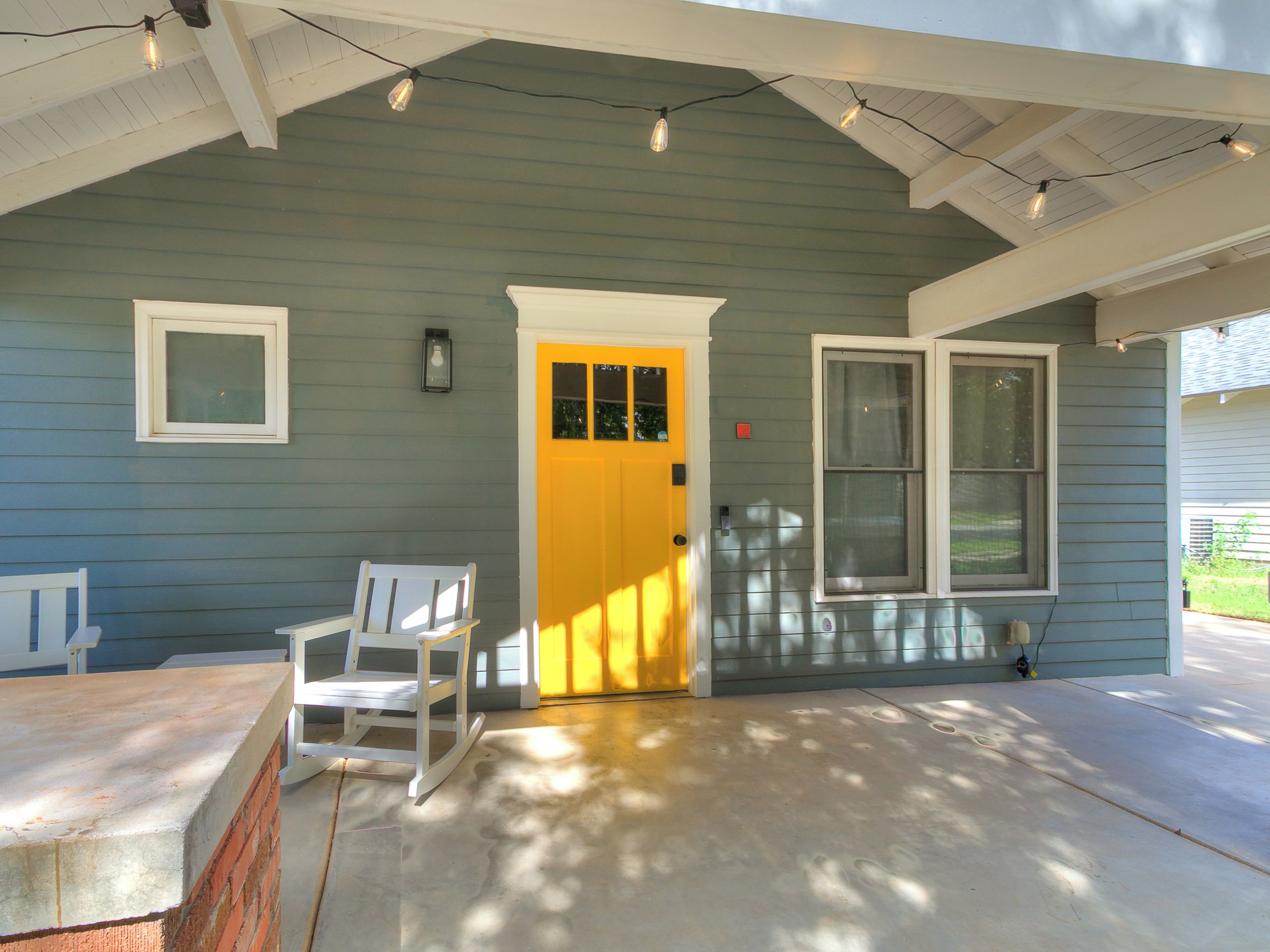 A house with a porch, a yellow door, a white chair, and a window.
