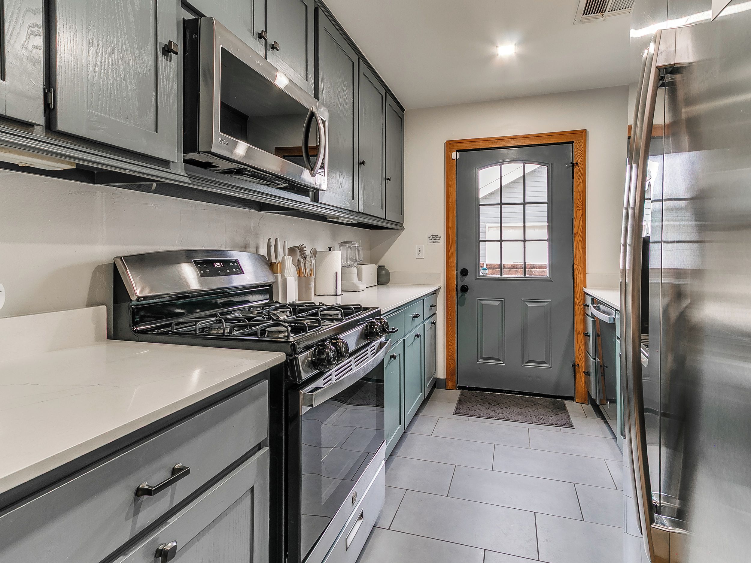 A kitchen with grey cabinets, a stainless steel refrigerator, and a microwave.