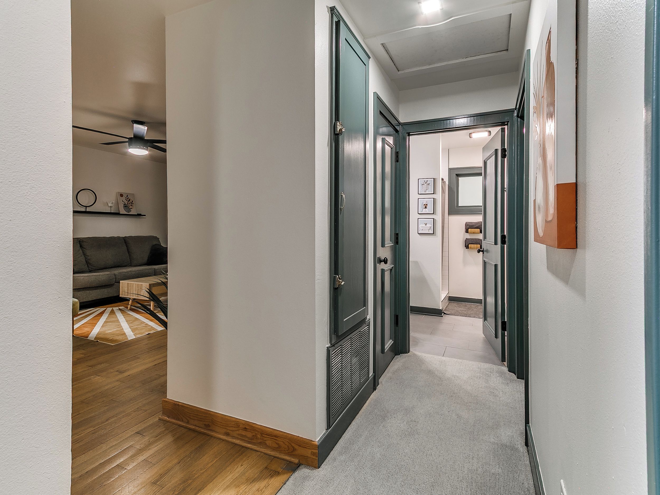 A hallway with a wooden floor, a grey carpet, and a grey door leading to a room.