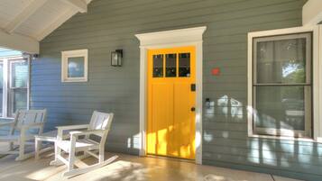 A porch with a yellow door, white rocking chairs, and a window.