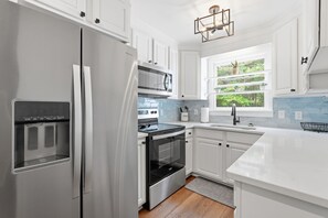 Cozinha moderna com eletrodomésticos de aço inoxidável, armários brancos, janela com vista para o verde e painel de parede azul claro.