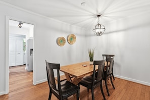 A dining area with a wooden table and four chairs, a hanging light fixture, and two wall-mounted decorative plates. - Lowcountry Cottage w/ Firepit - Near Downtown (Beaufort)