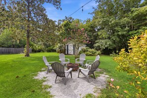 A patio with four Adirondack chairs, a fire pit, and a small shed in a lush garden. - Lowcountry Cottage w/ Firepit - Near Downtown (Beaufort)