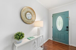 A hallway with a teal door, a white console table with a lamp, a mirror, and a small plant. - Lowcountry Cottage w/ Firepit - Near Downtown (Beaufort)