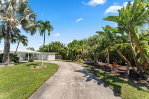 A residential property with a paved driveway, palm trees, and a house with a white exterior. - 2-bedroom townhome Island living Canal front Walk to the BEACH (Jensen Beach)