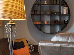 Ein rundes, gitterförmiges Bücherregal an einer Wand, eine Lampe und ein Sofa mit Kissen.