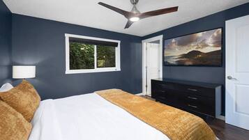 A bedroom with a bed, a ceiling fan, a dresser, a window, and a painting on the wall.