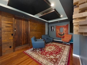 A room with a wooden floor, two blue armchairs, a red patterned rug, and a wooden wall panel.