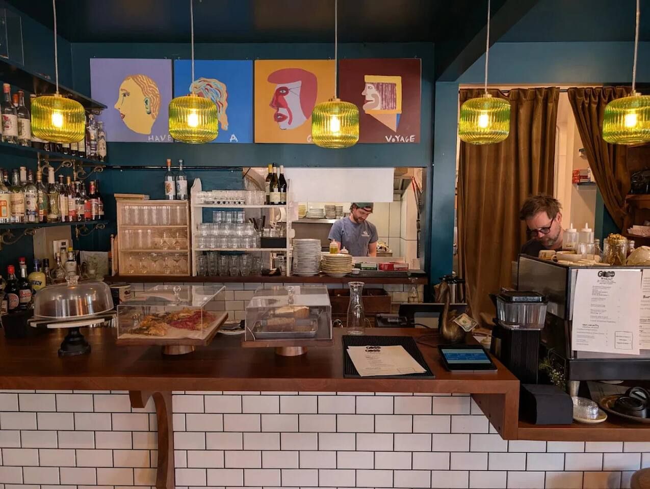 A bar area with a counter, shelves with bottles, and a menu board.