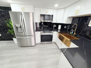 A modern kitchen with stainless steel appliances, white cabinetry, and a black countertop. - Spacious Black Luxe Retreat with 2 Kitchens, 2 Master Suites & Luxury Comfort (Tampa)